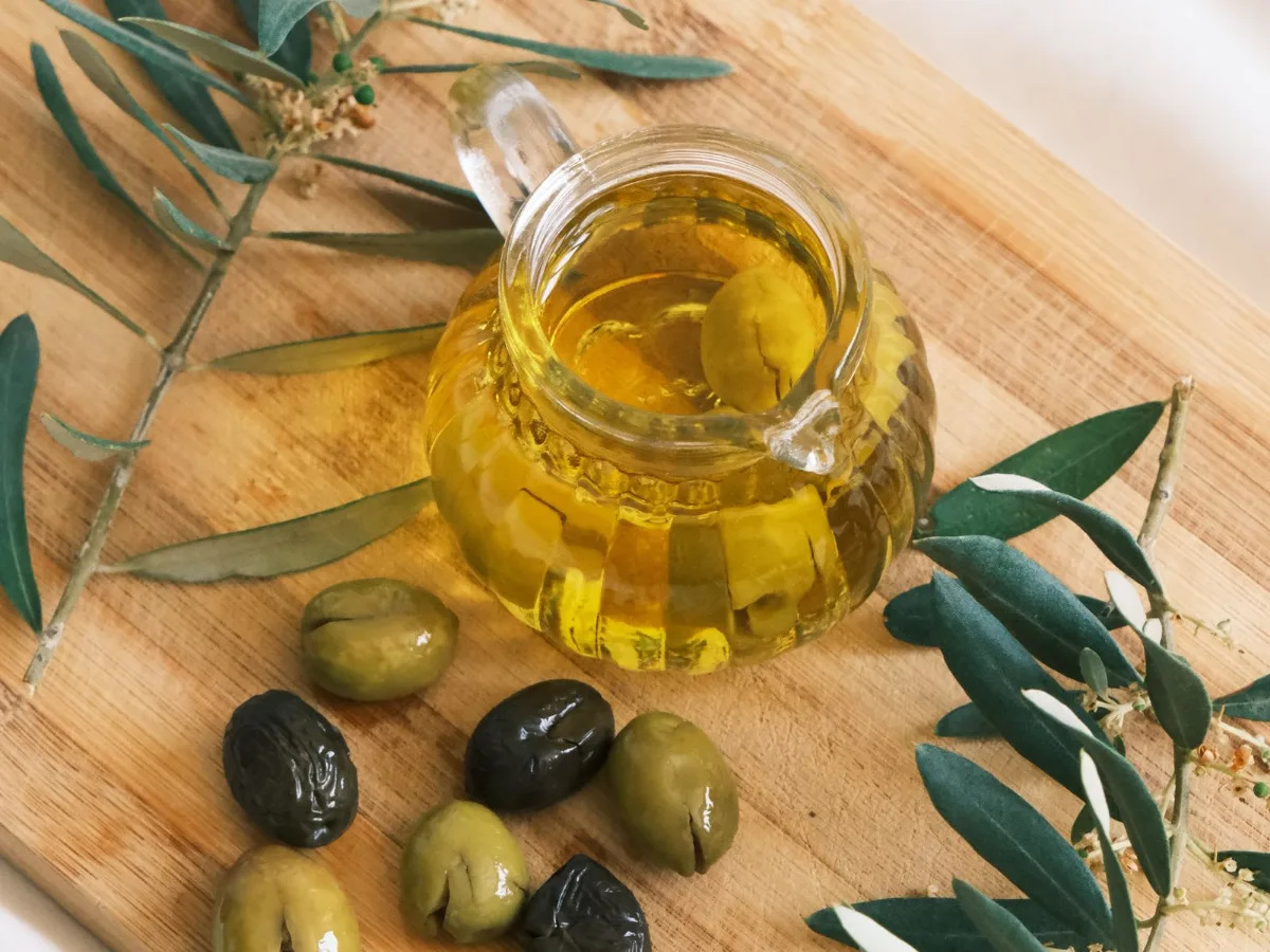 Carafe d'huile d'olive, olives et rameaux d'olivier sur une planche en bois